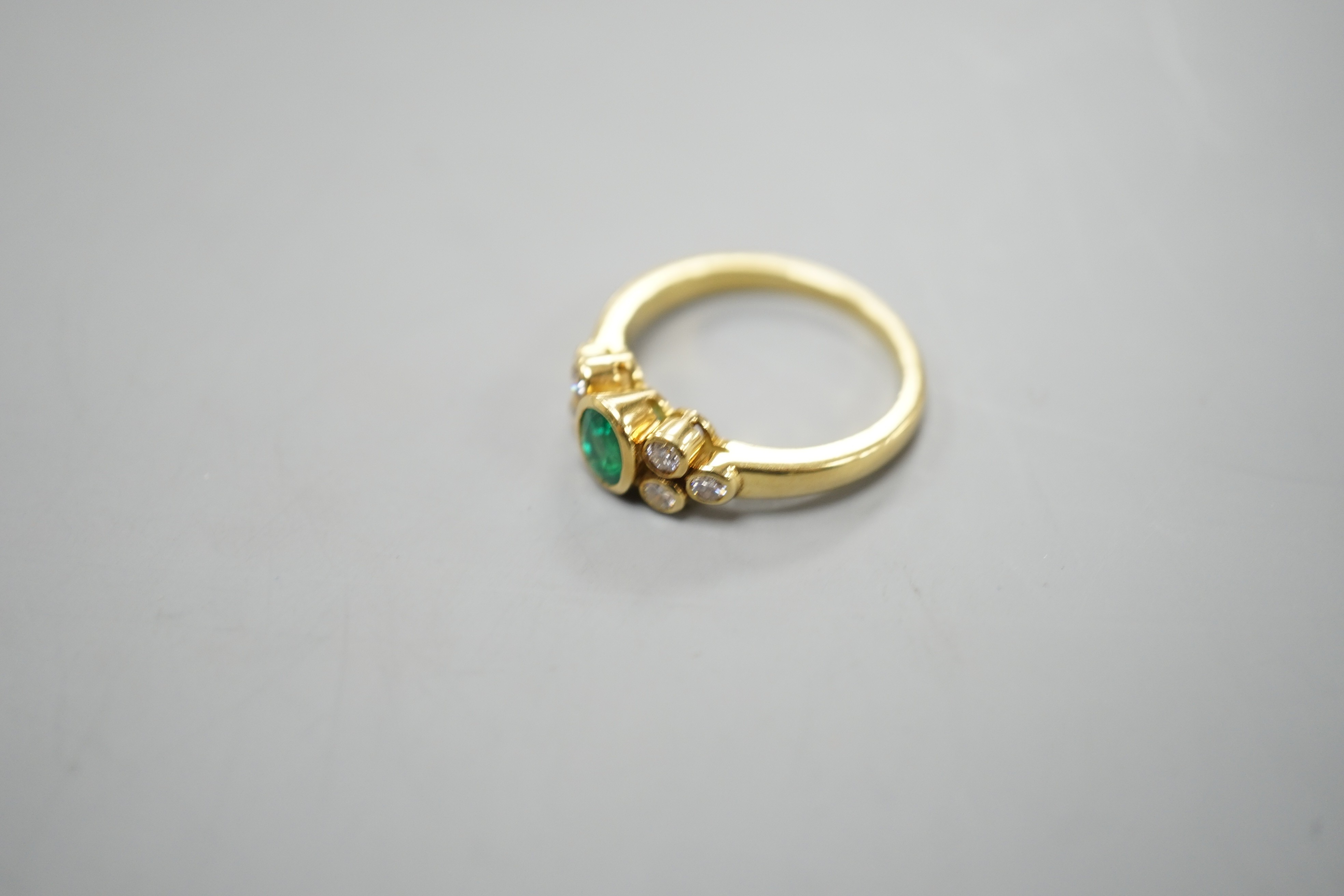 A modern yellow metal and collet set oval cut emerald ring, with six stone diamond set shoulders, size L/M, gross weight 4.1 grams.